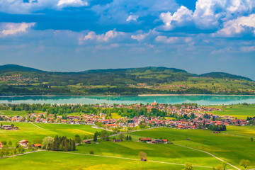 Fototapeta na wymiar Lovely panoramic view of the village Schwangau and the turquoise blue man-made lake Forggensee in Bavaria, Germany. The beautiful landscape view can be admired from the famous Neuschwanstein Castle.