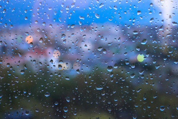 Raindrops on window glasses surface with blurred cityscape background
