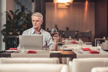 Fototapeta na wymiar Pleasant retired man drinking wine in a cafe