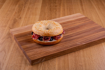 Roll with sesame, salami and olives on a wooden board