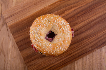 Round roll with sesame and sausage on a wooden board the top view