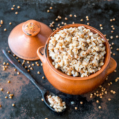 Freshly cooked buckwheat porridge in a small brown clay pot on a dark background. 