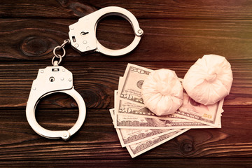 iron handcuffs for the arrest of criminals, us dollar bills, drugs on the background of a wooden...