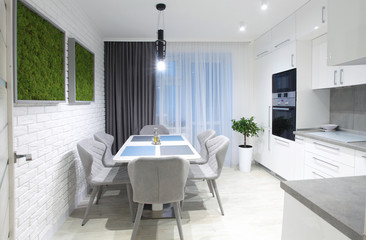 White kitchen interior with grey chairs,moss on the wall in new luxury home with lights on