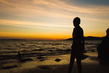 Child playing with sun is hiding the beach edge with orange sky