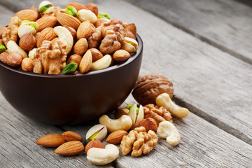 Naklejka na ściany i meble Wooden bowl with mixed nuts on a wooden gray background. Walnut, pistachios, almonds, hazelnuts and cashews, walnut.