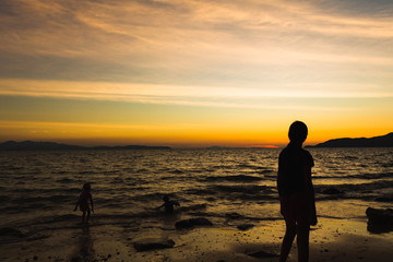 Fototapeta na wymiar Child playing with sun is hiding the beach edge with orange sky