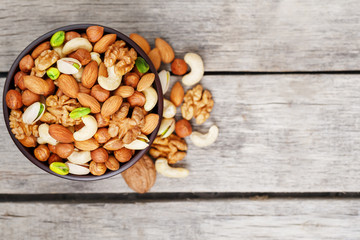 Wooden bowl with mixed nuts on a wooden gray background. Walnut, pistachios, almonds, hazelnuts and cashews, walnut.