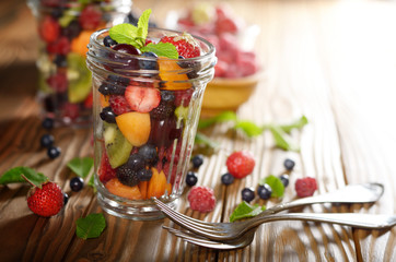 Assorted berries in mason jar on kitchen wooden table with fork aside