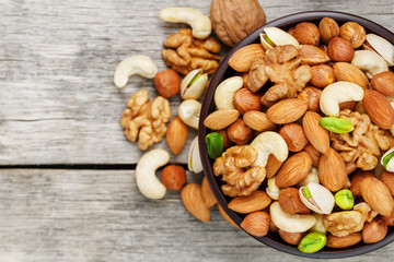 Wooden bowl with mixed nuts on a wooden gray background. Walnut, pistachios, almonds, hazelnuts and cashews, walnut.