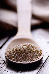 Raw organic superfood gluten free quinoa seeds in wooden spoon on kitchen table closeup
