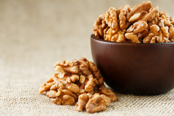 Peeled walnuts in a wooden, dark brown cup on a burlap cloth.