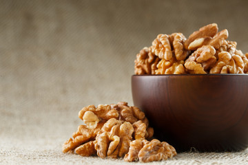 Peeled walnuts in a wooden, dark brown cup on a burlap cloth.