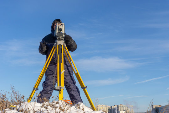 Surveyor conducts a topographical survey in winter for cadastral work at a construction site