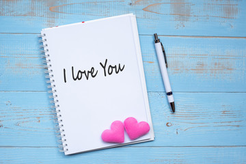 I LOVE YOU word on notebook and pen with couple pink heart shape decoration on blue wooden table background. Wedding, Romantic and Happy Valentine’ s day holiday concept