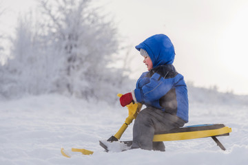 little child riding a snow scooter in winter