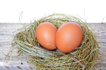 Two red chicken eggs in a straw nest on a rough wooden Board on a white background