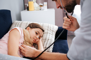 Obraz premium Cut view of young male doctor listen to small girls breathing through stethoscope. She lying on bed.