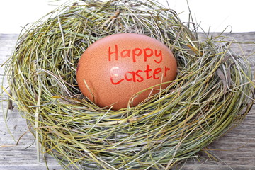 Red chicken eggs in a straw nest on a rough wooden Board with text happy easter on a white background. Close up