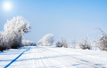 Obraz premium Countryside road through winter field with forest on a horizon. Winter landscape countryside, forest, field.