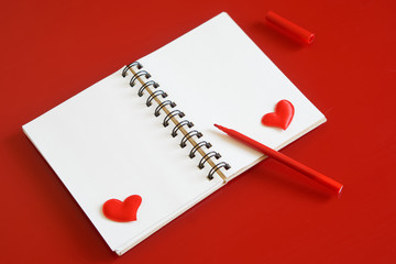 Notepad with hearts and a red felt-tip pen on a red background. Diagonal arrangement. Preparation for congratulations on Valentine's Day