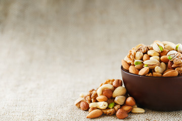 Mix of different nuts in a wooden cup against the background of fabric from burlap. Nuts as structure and background, macro. Top view.