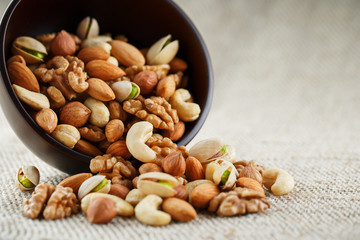 Mix of different nuts in a wooden cup against the background of fabric from burlap. Nuts as structure and background, macro. Top view.