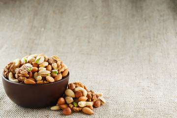 Mix of different nuts in a wooden cup against the background of fabric from burlap. Nuts as structure and background, macro. Top view.