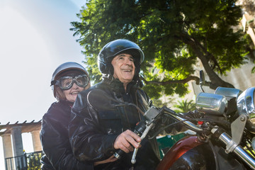 coppia di motociclisti anziani in sella a una moto sorridono divertiti con i caschi