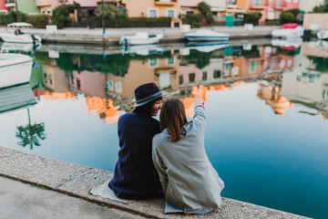 Two happy friends sitting on the dock at the port, having fun and talking on the street. Lifestyle outdoors
