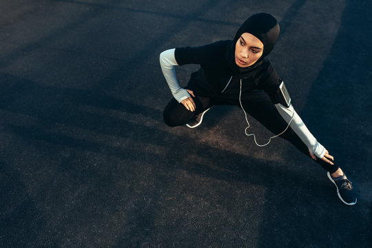 Woman wearing Muslimah sportswear stretching outdoors - Powered by Adobe