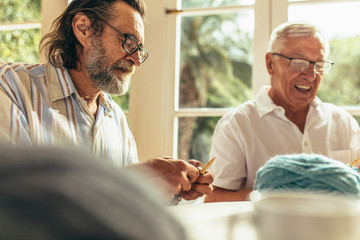 Obraz premium Senior beard man knitting with friend sitting by