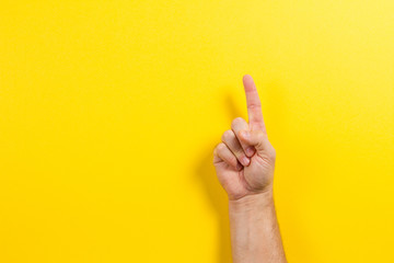 Man hand showing one finger on yellow background