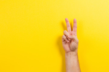 Man hand showing two fingers on yellow background. Number two symbol