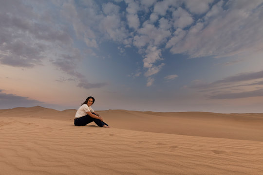 Woman sitting on a dune in the desert enjoying the sunset