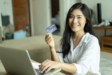 Young Asian Thai woman holding a credit card and using laptop computer for buying purchase online...