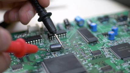 Computer engineer with tester examining green motherboard with processor, chips and capacitors