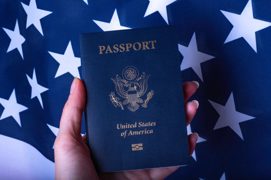 Female hand holding Passport of USA on American flag background.