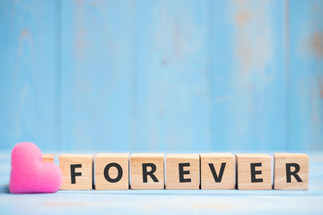 FOREVER wooden cubes with pink heart shape decoration on blue table background and copy space for text. Love, Romantic and Happy Valentine’s day holiday concept