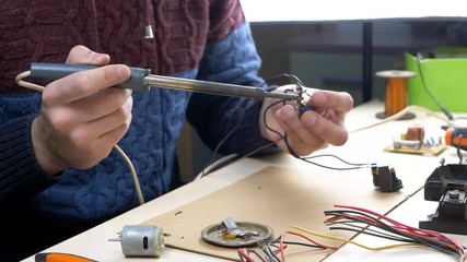 Repair of electronic devices, tin soldering parts in electronics workshop with PC matherboards background