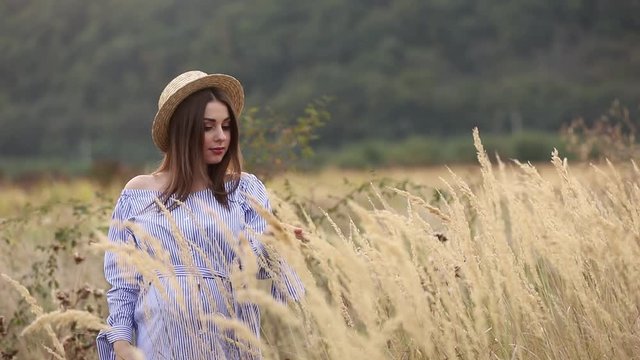 Pregnant woman in nature try on knitted hat. Background of field and white fance near the farm. mountains