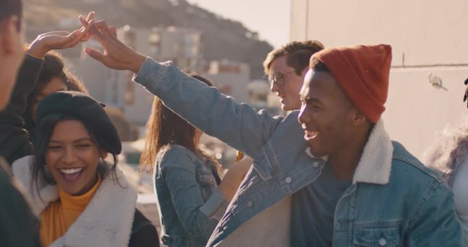 slow motion multi ethnic friends enjoying rooftop party celebration dancing together enjoying summer vacation drinking alcohol celebrating on sunny weekend in urban city at sunset