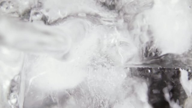 Carbonated clear water pour into a glass of ice cubes with bubbles top view