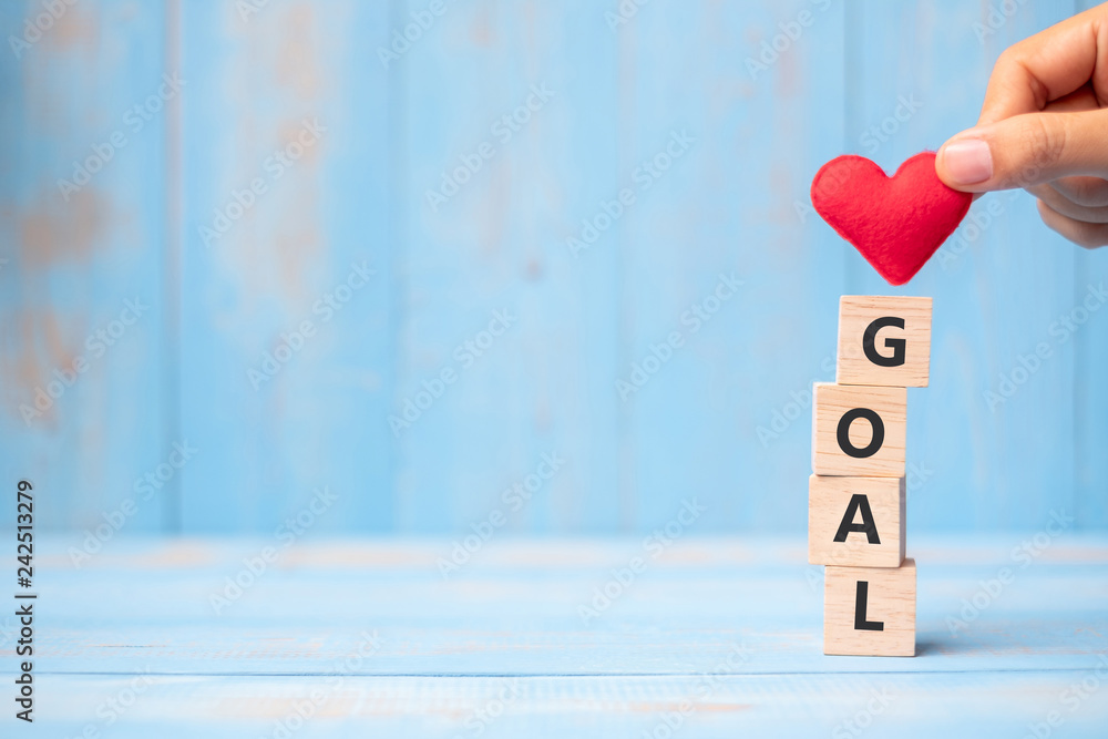 Wall mural business man hand holding red heart shape over goal wooden cubes on blue table background with copy 