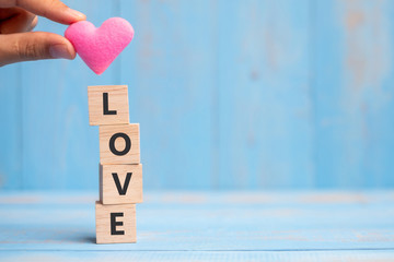 LOVE wooden cubes with pink heart shape decoration on blue table background and copy space for text. Love, Romantic and Happy Valentine’s day holiday concept