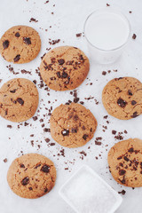 Homemade chocolate chips cookies with salt on small plate and glass of milk on white background, top view. Food styling shot