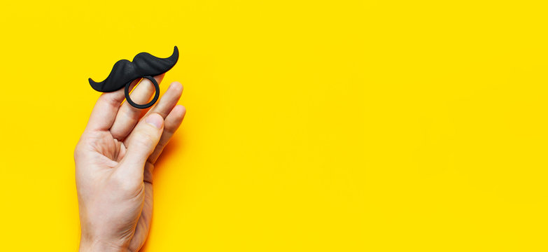 Men's hands hold Black mustache, props for photo booths, carnival, parties on yellow background top view flat lay copy space Father's day Creative party decoration concept