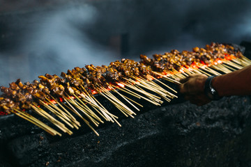 Roasting meat, chicken and mutton satays with charcoal, fire and smoke at night market in Jakarta,...