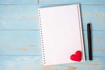 Blank notebook and pen with couple red heart shape decoration on blue wooden table background. Wedding, Romantic and Happy Valentine’ s day holiday concept