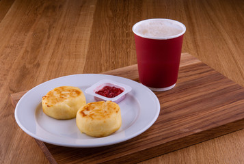 Cherry jam with cheesecakes on a plate, is served with a cup of coffee